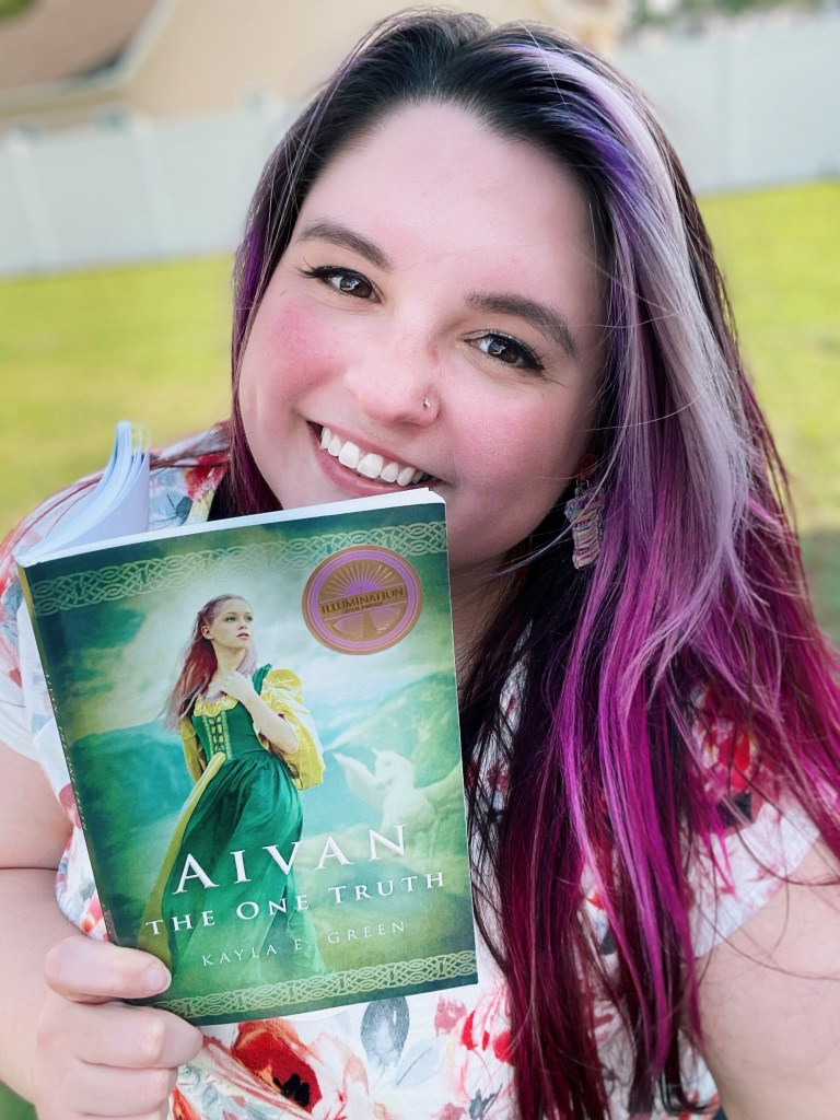 Author Kayla E. Green smiles with her book Aivan: The One Truth.