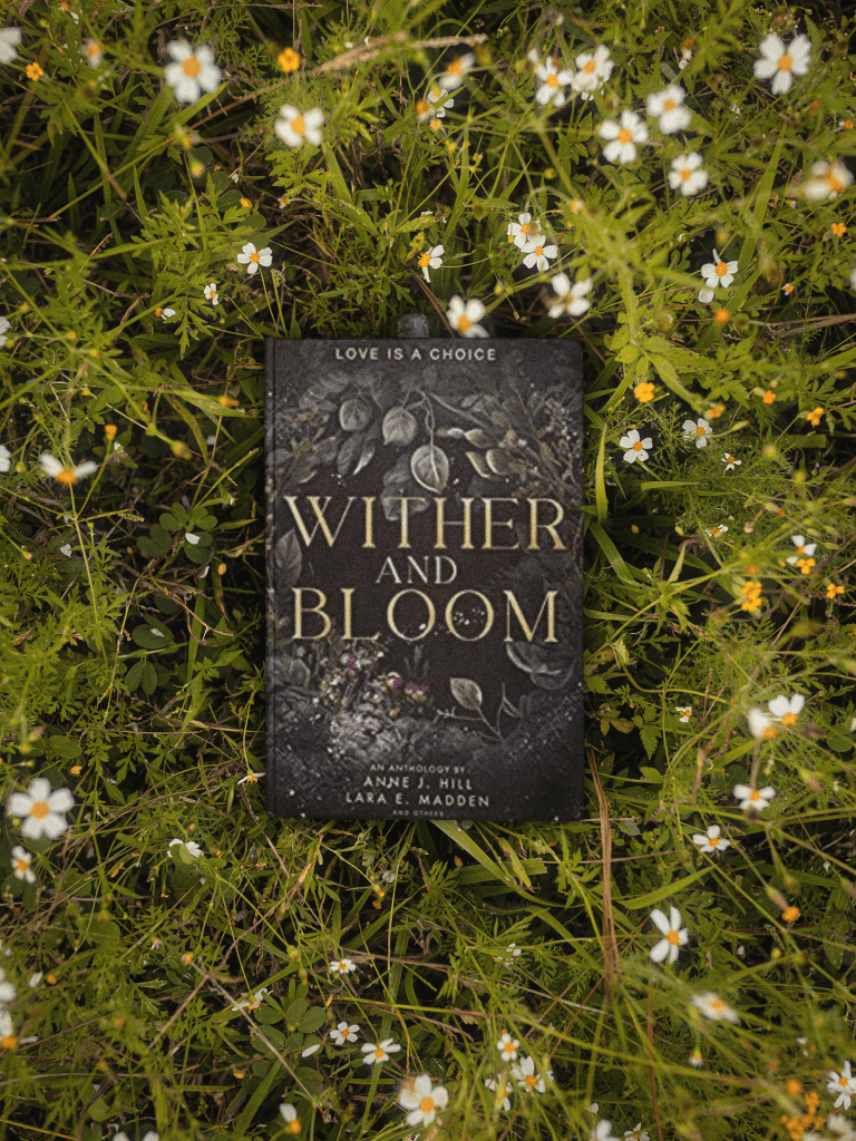 Copy of the book Wither and Bloom sites in grass with little white flowers.