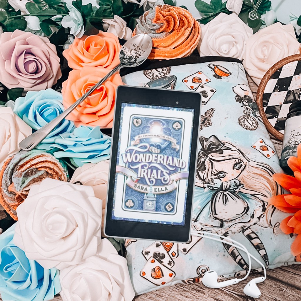 Phone with "The Wonderland Trials" book on the screen laid over headphones and a cartoon Alice book sleeve.